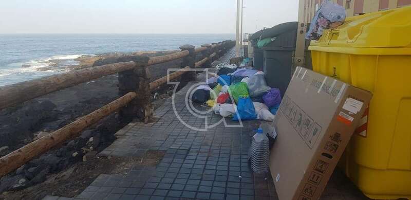 Basura acumulada sobre la acera junto a contenedores repletos de residuos/TA.